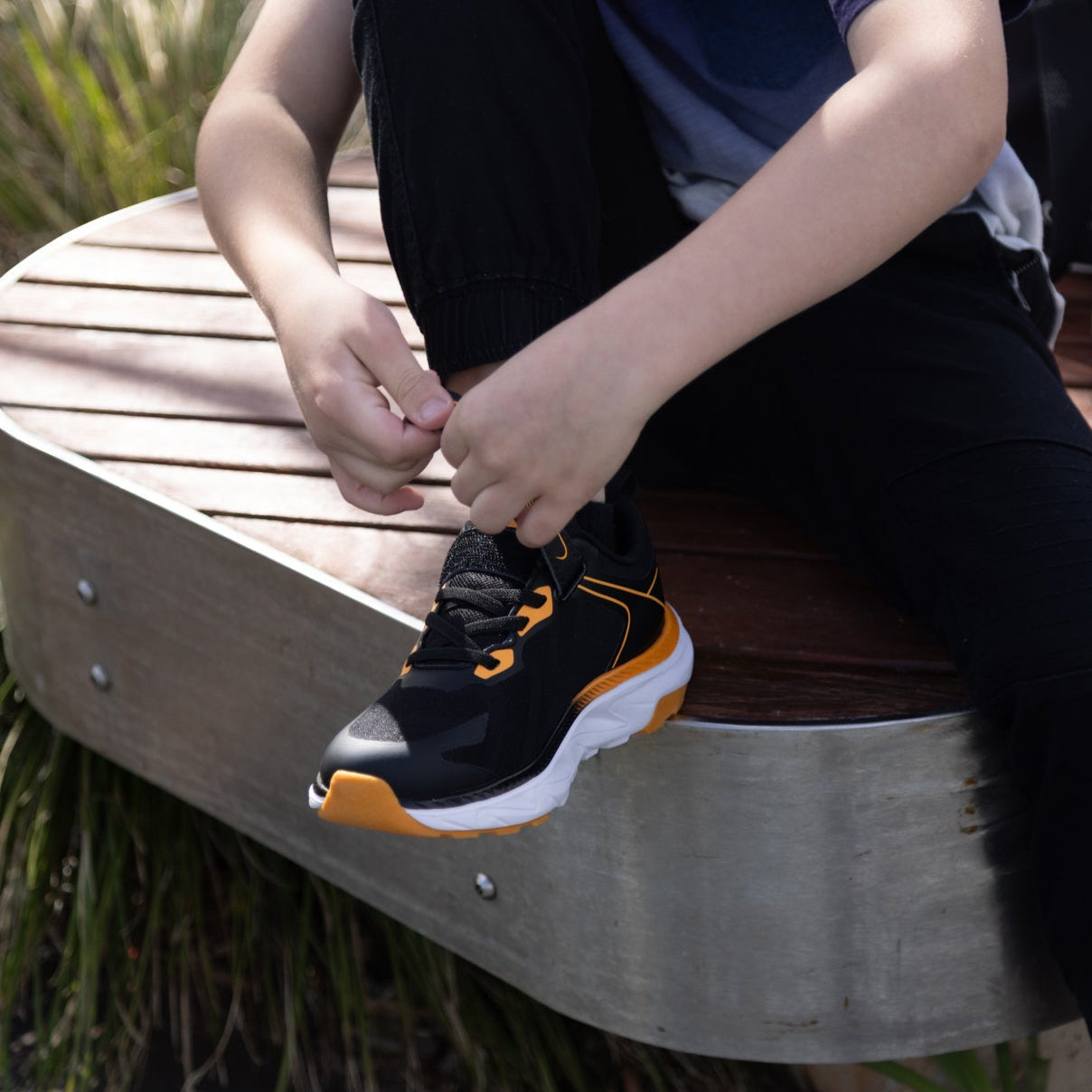 Child sitting on a wooden bench tying shoelaces outdoors