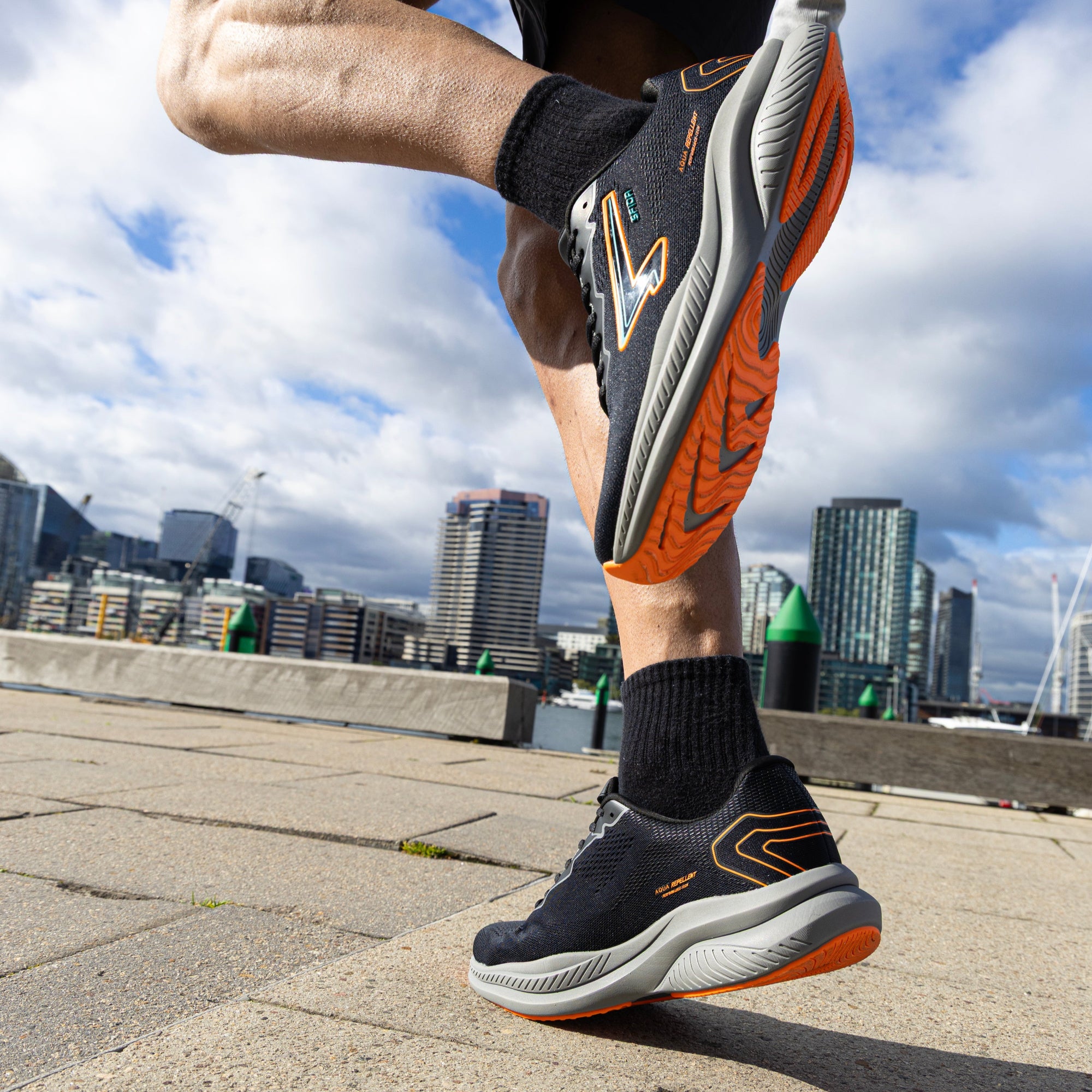 Person running on a city street wearing black and orange running shoes.