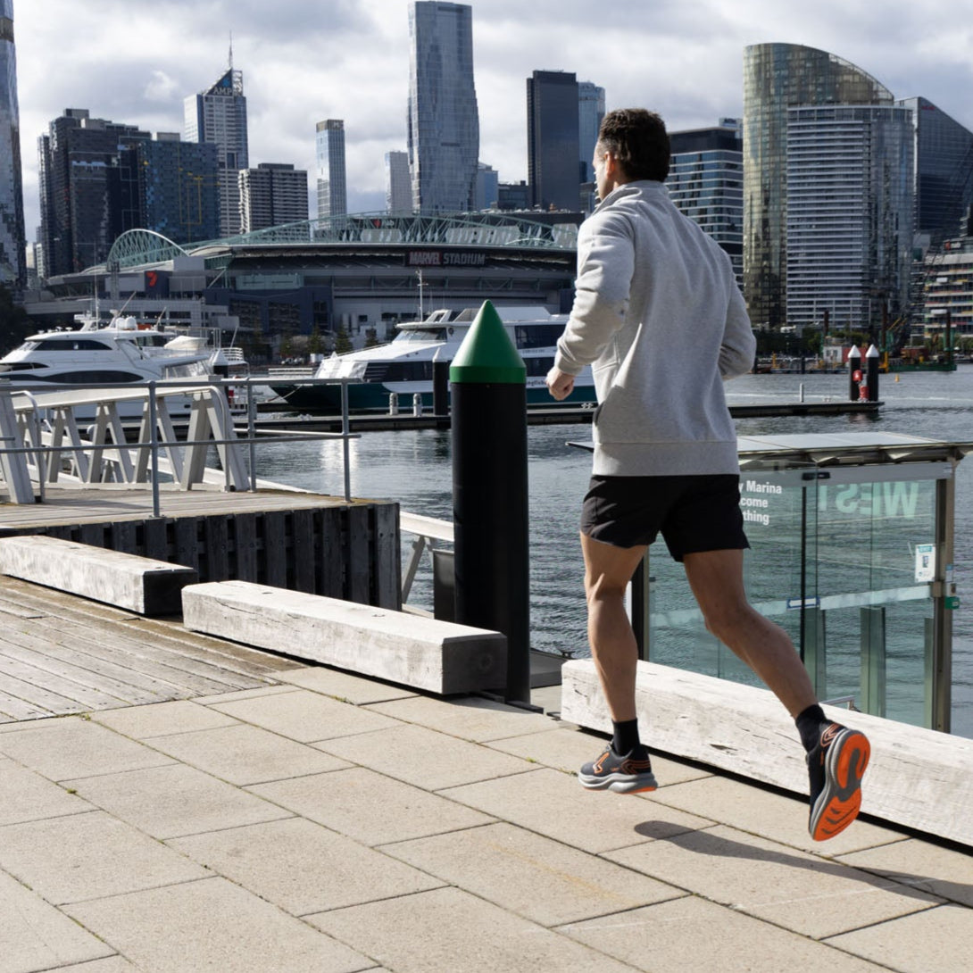 Person running along a waterfront promenade with a city skyline in the background