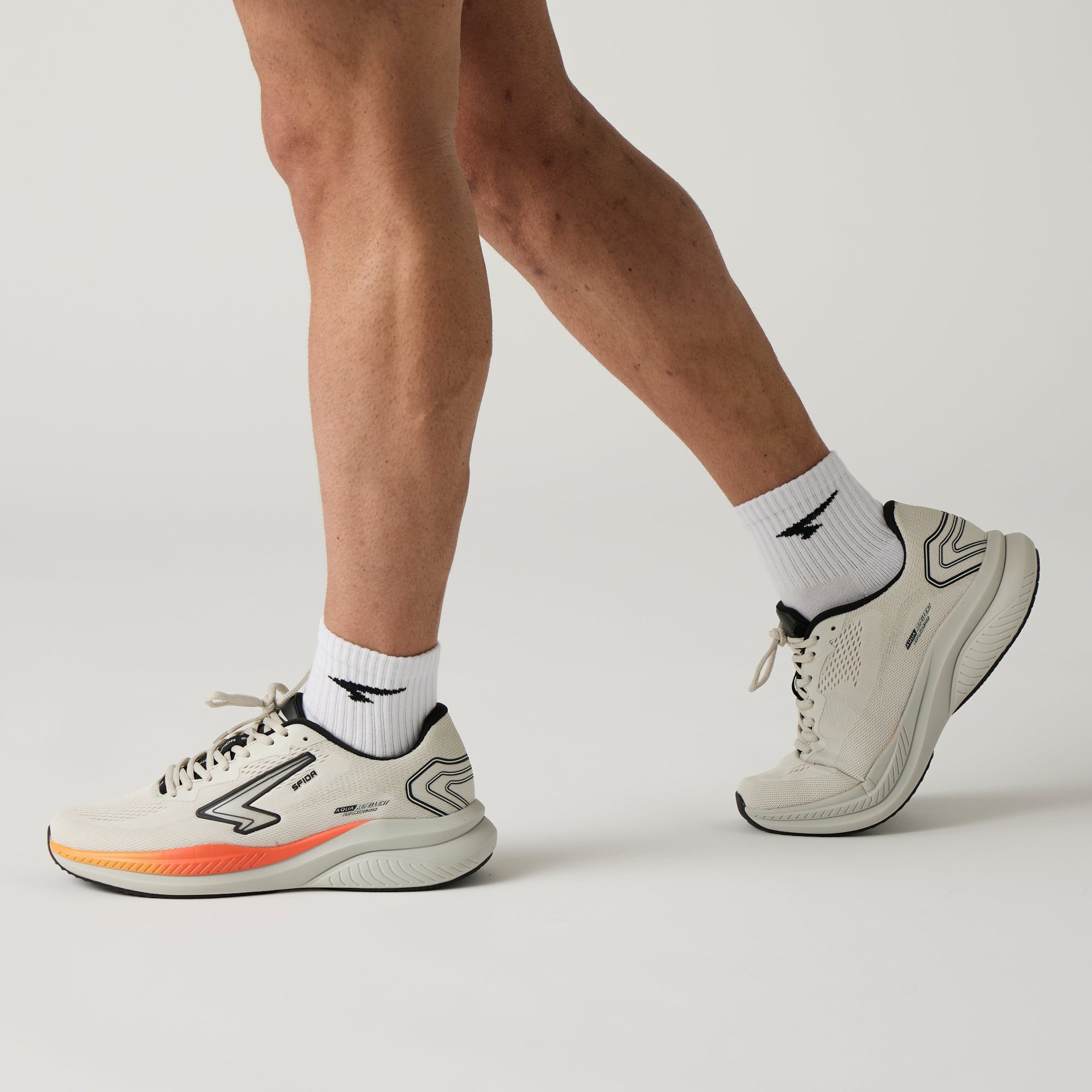 Person wearing light grey athletic shoes with colourful sole on a light grey background