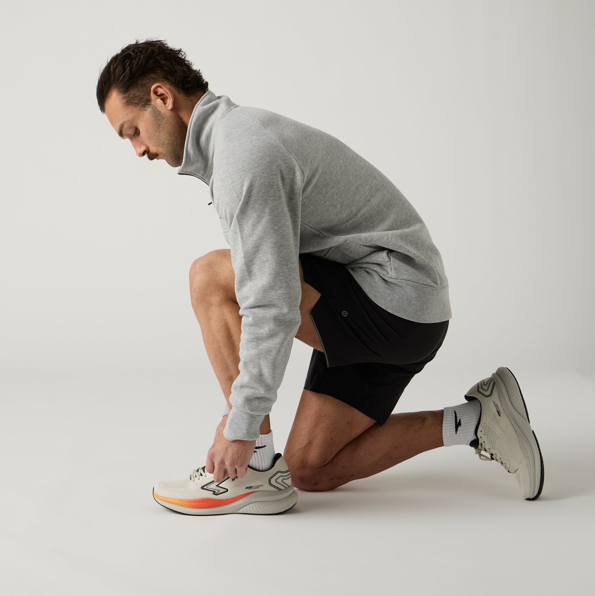 Man tying his running shoes on a plain background