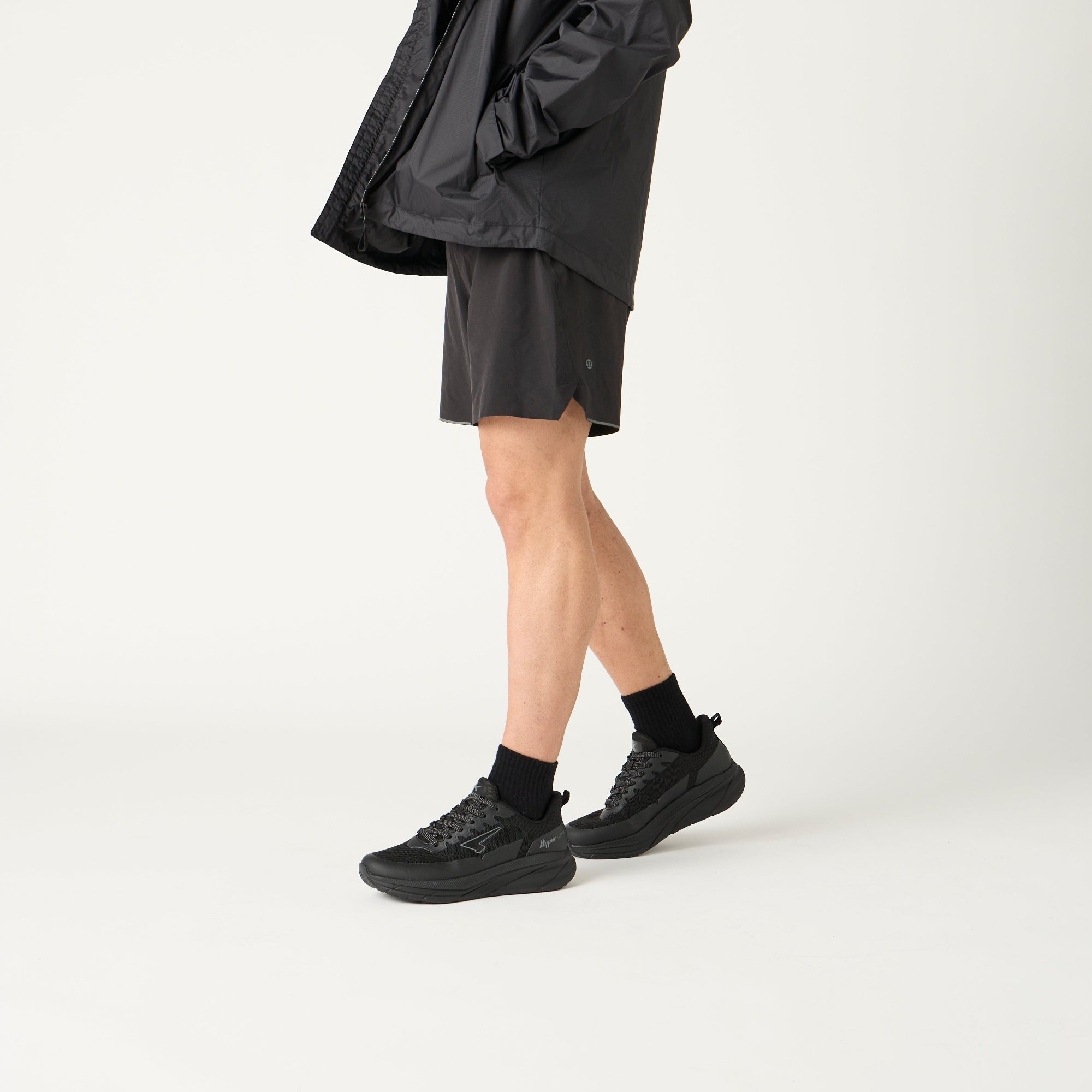 Person wearing a black raincoat and shorts on a white background