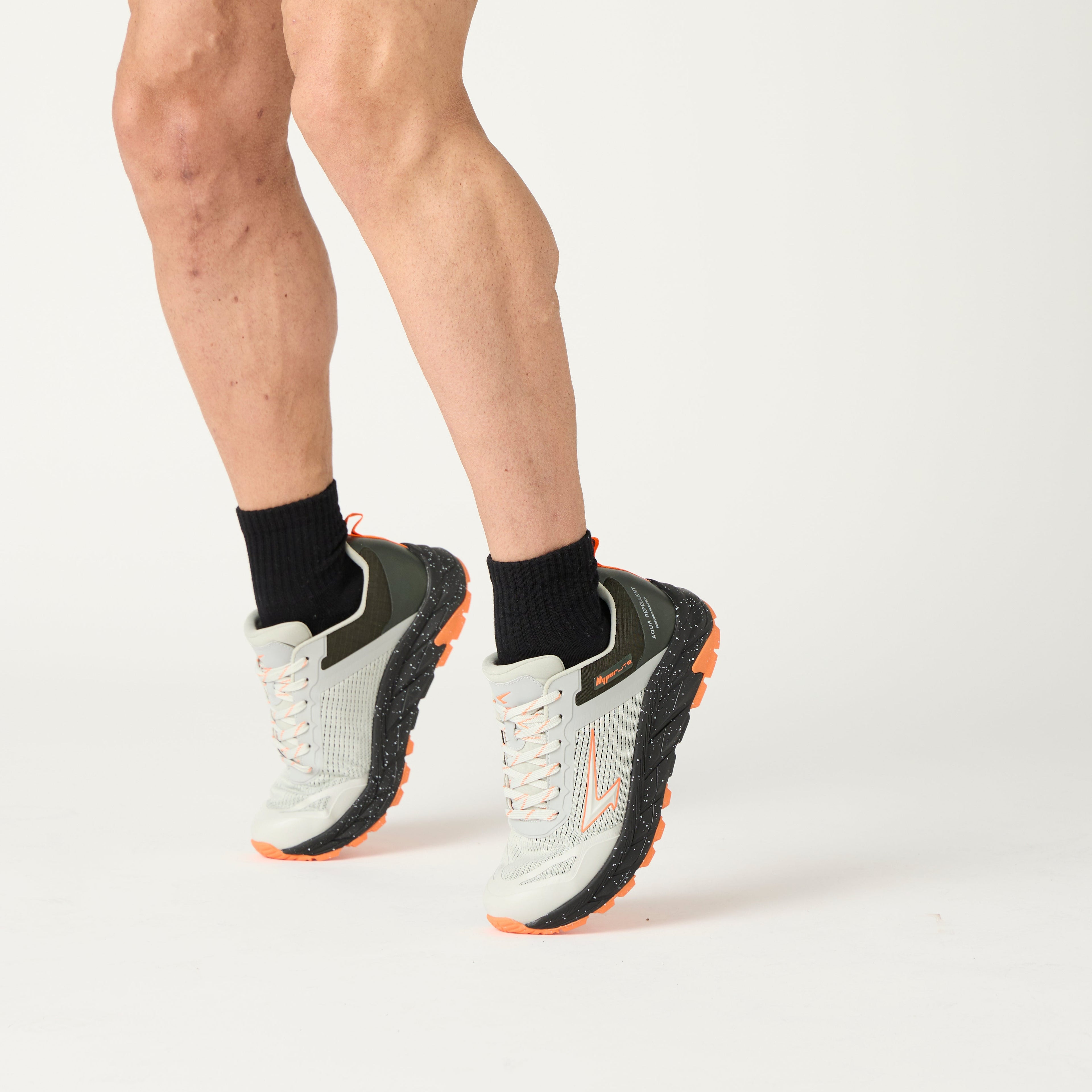 Person wearing black athletic shorts, black socks, and light grey trail running shoes on a white background