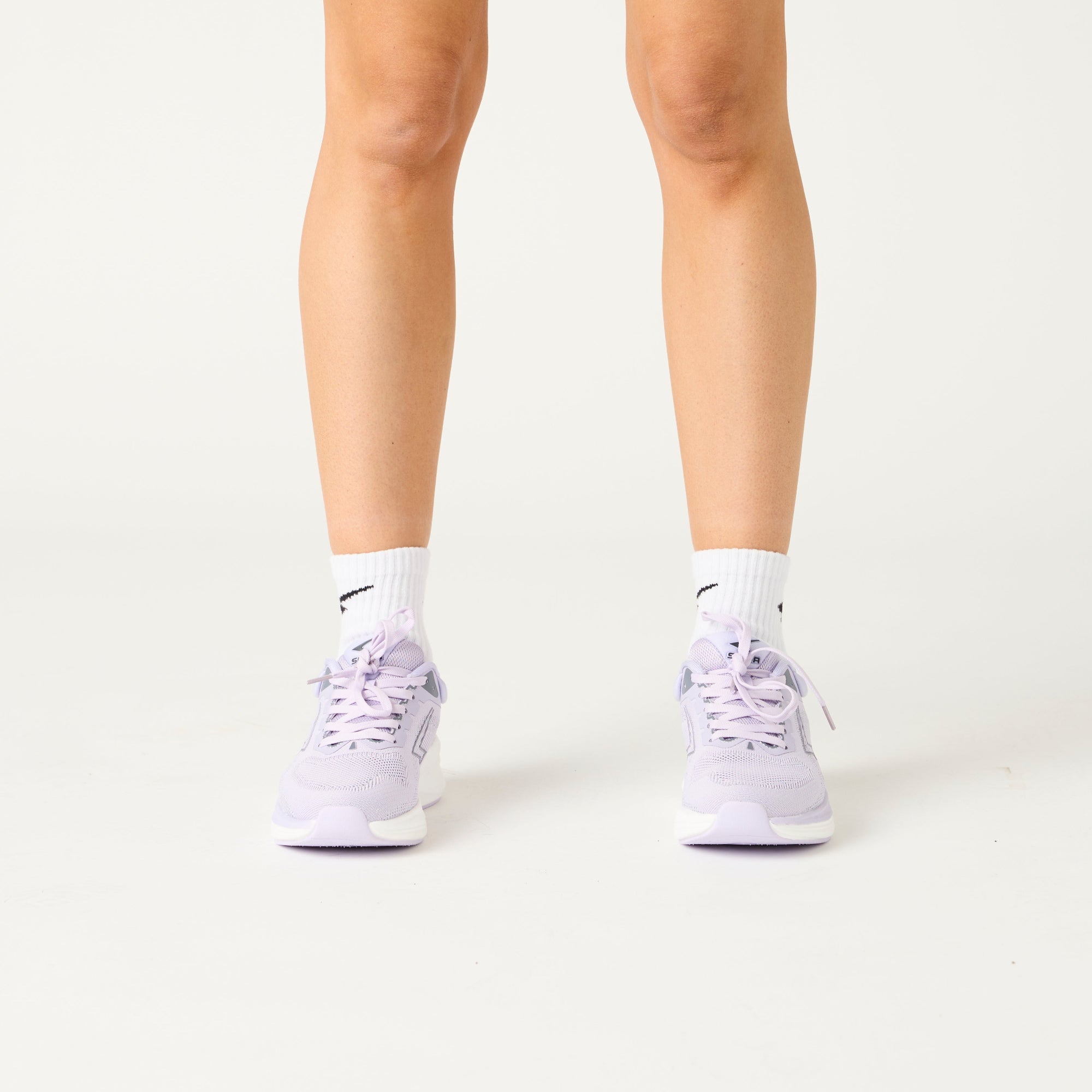 Person wearing light purple sneakers and white socks on a plain background