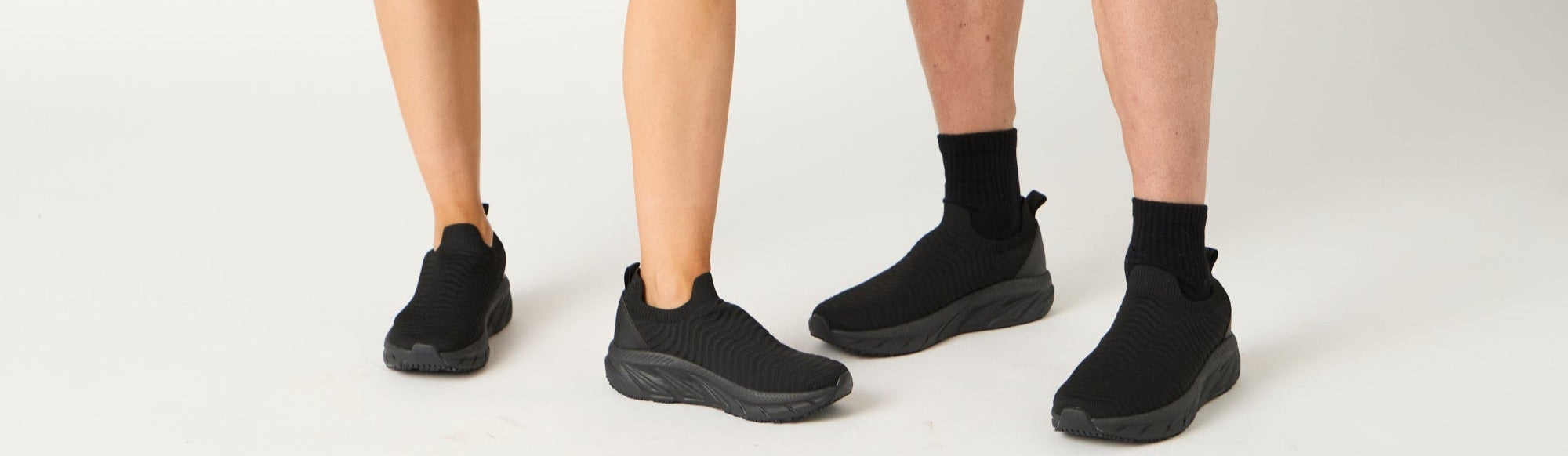 Two people wearing matching gray sweatshirts and black shorts with lifestyle sneakers on a white background