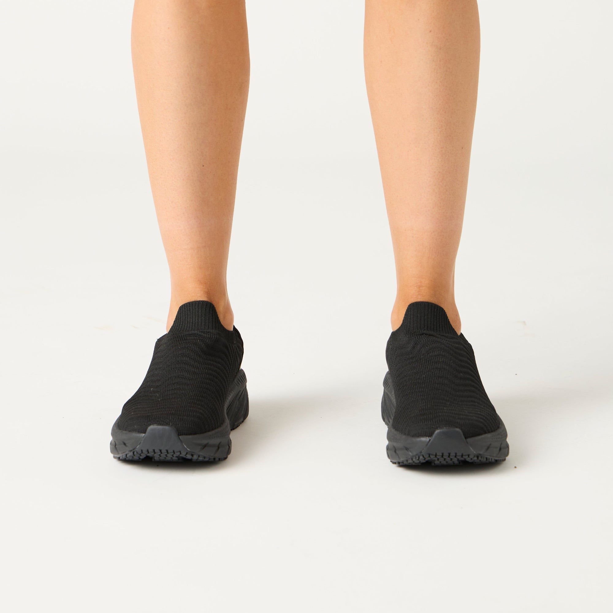 Black slip-on shoes worn by a person on a white background