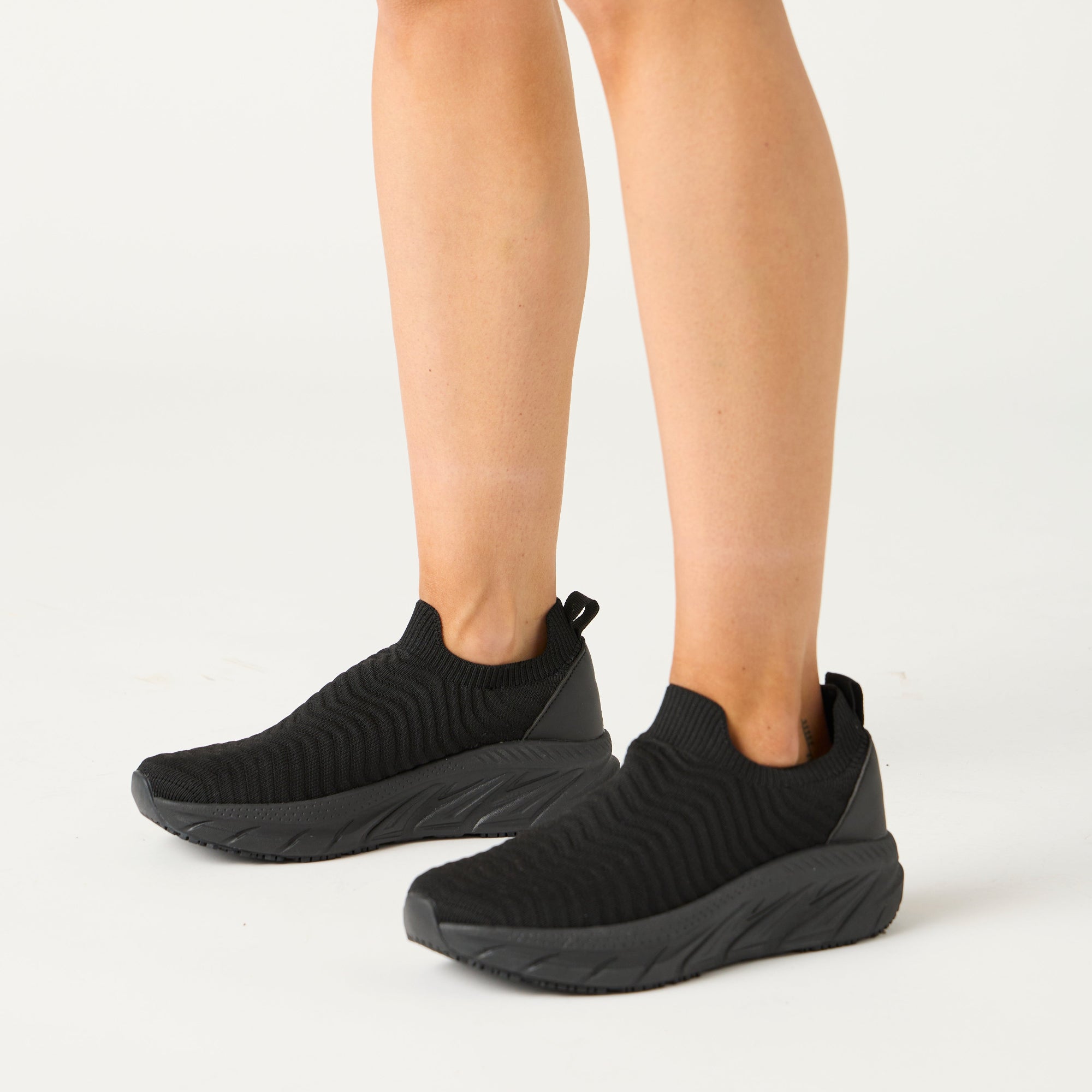 Black knit sneakers worn by a woman on a white background